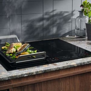 Sleek induction cooktop with fish grilling tray on a modern kitchen countertop, demonstrating Samsung Vietnam warranty service.