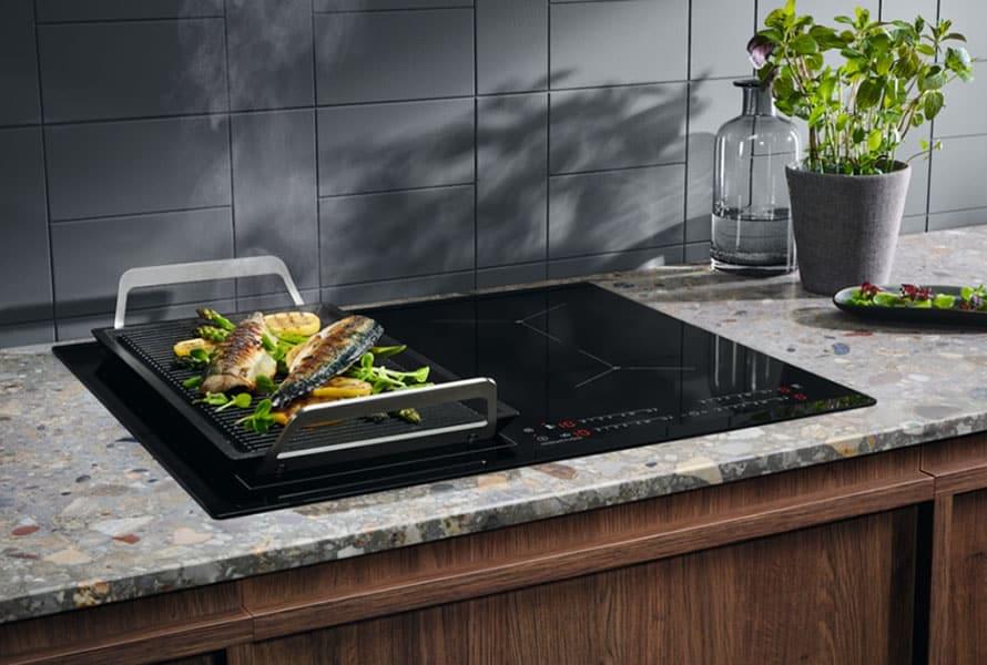 Sleek induction cooktop with fish grilling tray on a modern kitchen countertop, demonstrating Samsung Vietnam warranty service.